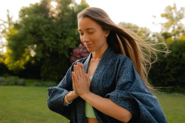 Kadın halka açık bir parkta yoga ve meditasyon yapıyor, gözleri kapalı rahatlıyor. Dikkatli meditasyon konsepti. Sağlıklı olmak. Odak bulanıklığı ve gürültü etkisi yok. Dizinin bir parçası.