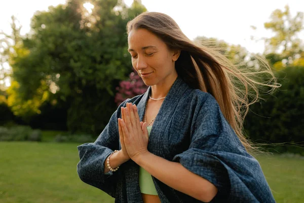 Kadın halka açık bir parkta yoga ve meditasyon yapıyor, gözleri kapalı rahatlıyor. Dikkatli meditasyon konsepti. Sağlıklı olmak. Odak bulanıklığı ve gürültü etkisi yok. Dizinin bir parçası.