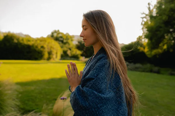 Kadın halka açık bir parkta yoga ve meditasyon yapıyor, gözleri kapalı rahatlıyor. Dikkatli meditasyon konsepti. Sağlıklı olmak. Odak bulanıklığı ve gürültü etkisi yok. Dizinin bir parçası.