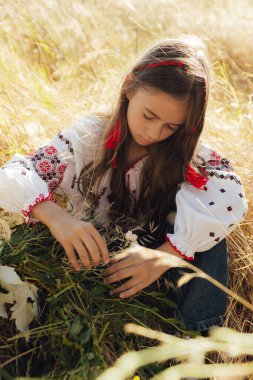 Geleneksel Vyshyvanka bluzlu Ukraynalı kızın Ivana Kupala kutlaması için çiçek çelengi dokuduğu yakın plan. Halk kostümü, yaz ortası Slav bayramı, kültür geleneği. Dizinin bir parçası.