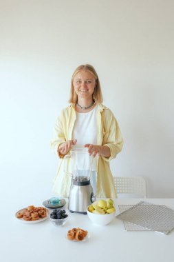 Beyaz kadın ev yapımı meyve derisi hazırlıyor, sağlıklı bir atıştırmalık için mutfağında taze meyve dilimliyor. Organik ikramlar ve doğal yaşam üzerine bir serinin parçası. Bir serinin parçası.