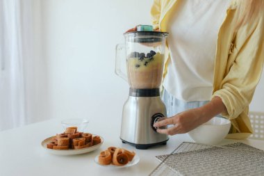 Ev yapımı meyve derisi hazırlayan, sağlıklı bir atıştırmalık için mutfağında taze meyve dilimleyen bir kadın. Organik ikramlar ve doğal yaşam üzerine bir serinin parçası. Bir serinin parçası.