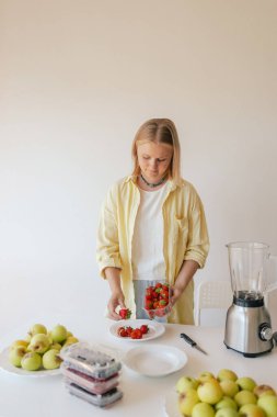 Beyaz kadın ev yapımı meyve derisi hazırlıyor, sağlıklı bir atıştırmalık için mutfağında taze meyve dilimliyor. Organik ikramlar ve doğal yaşam üzerine bir dizi..