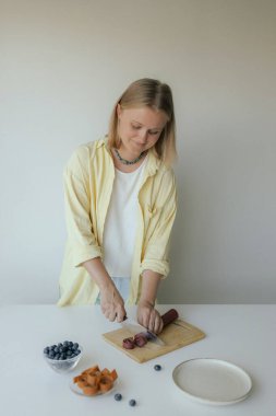 Beyaz kadın ev yapımı meyve derisi hazırlıyor, sağlıklı bir atıştırmalık için mutfağında taze meyve dilimliyor. Organik ikramlar ve doğal yaşam üzerine bir dizi..