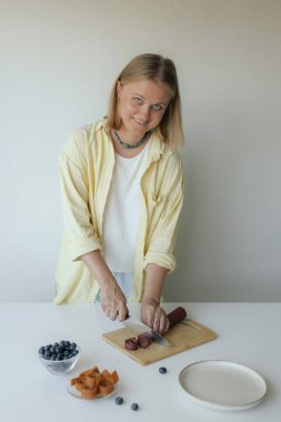 Beyaz kadın ev yapımı meyve derisi hazırlıyor, sağlıklı bir atıştırmalık için mutfağında taze meyve dilimliyor. Organik ikramlar ve doğal yaşam üzerine bir dizi..