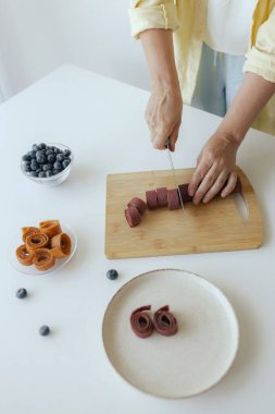 Beyaz kadın ev yapımı meyve derisi hazırlıyor, sağlıklı bir atıştırmalık için mutfağında taze meyve dilimliyor. Organik ikramlar ve doğal yaşam üzerine bir dizi..