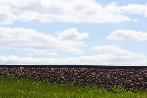 Mavi gökyüzünün arka planındaki demiryolu raylarının yan görüntüsü mesafeyi gösteriyor. Yol kenarı taşlarla dolu. Ücretsiz seyahat kavramı