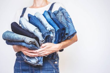 The girl holds a stack of jeans in her hands. cleaning in the closet clipart