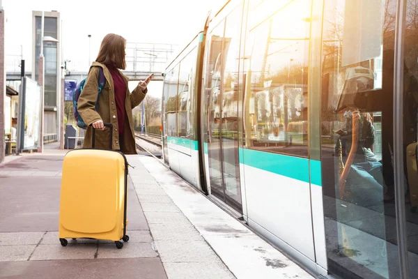 女孩游客与背包和一个大黄色的手提箱站在平台上 等待火车 — 图库照片
