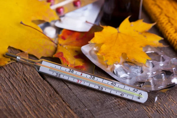 Fall and health care. cup of tea, pills and thermometer on a wooden backgroun