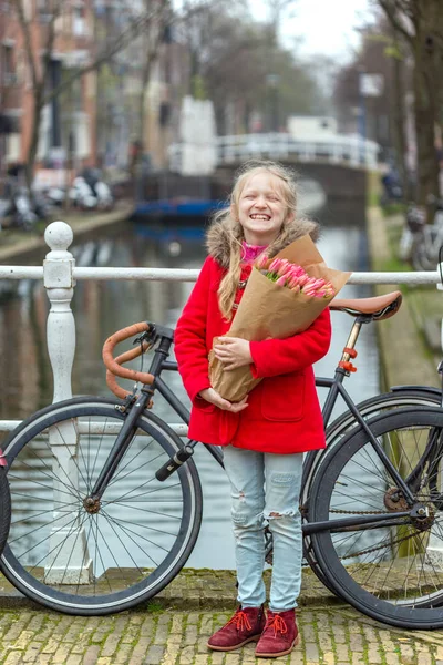 幸福的微笑的小女孩拿着一束郁金香站在阿姆斯特丹的街道上 — 图库照片