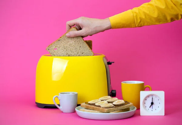 有趣的早餐 准备敬酒的女孩 黄色烤面包机和一杯粉红色背景上的咖啡 — 图库照片