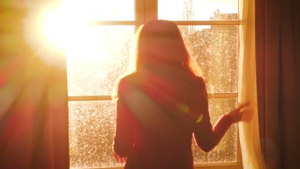 Flicka Öppnar Ett Fönster Och Tittar Kvällen Staden Strålar Orange — Stockvideo