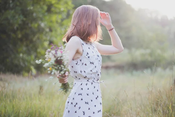 花束を持つ少女が牧草地を歩く 夏の気分とインスピレーションは — ストック写真