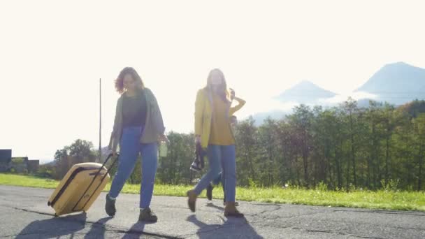 ヨーロッパアルプスの日当たりの良い田舎道を歩く荷物を持つ3人の笑顔の観光客の女の子 — ストック動画