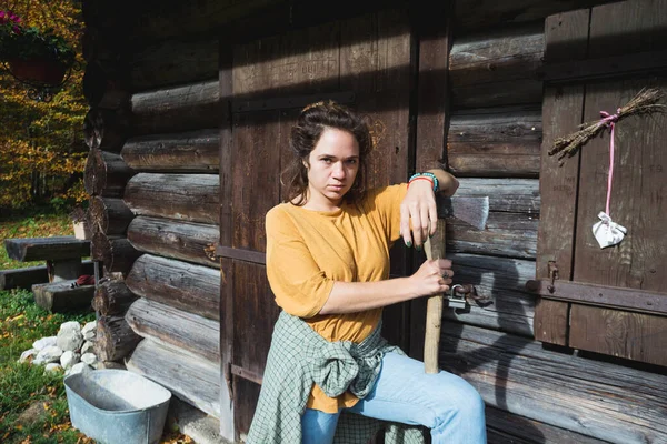 在山上一座木头房子附近拿着斧头的女孩 — 图库照片