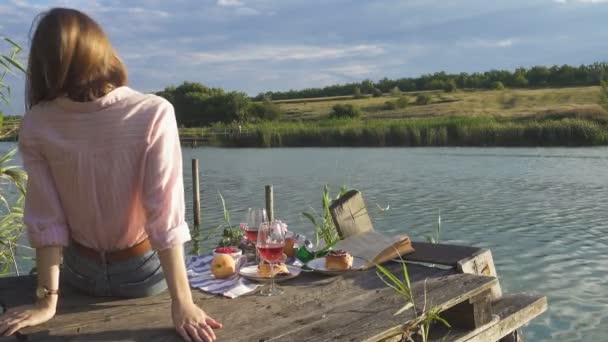 女孩喜欢在夏日明媚的河岸上的木制码头野餐 — 图库视频影像