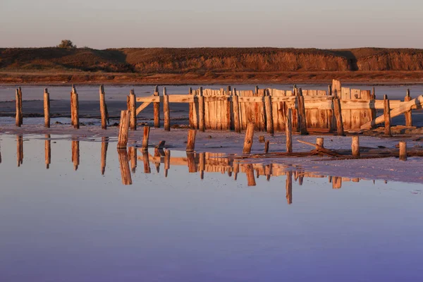 夜明けにピンク色の塩湖の美しい風景 破壊されたダムの木造遺跡 — ストック写真