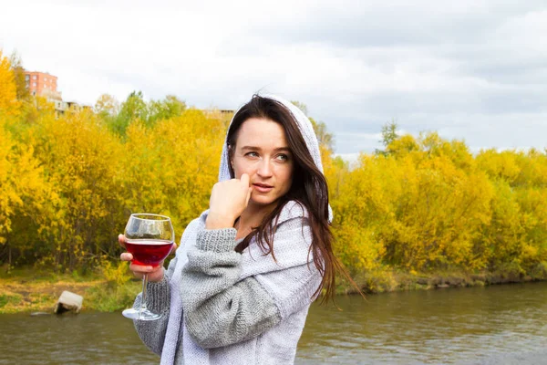 Young girl with a glass of wine on the river bank