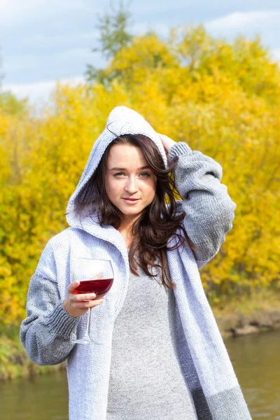 Girl with a glass of wine on the river bank. Autumn