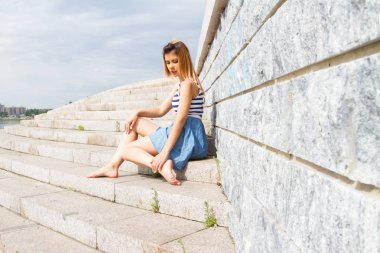Genç kız taş bir duvara yaslanmış merdiven beton adımlardan oturur
