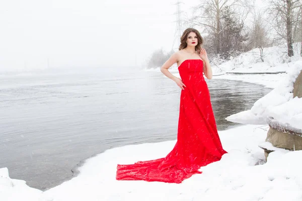 Młoda Dziewczyna Czerwonej Sukience Stoi Brzegu Rzeki Pokrytych Śniegiem — Zdjęcie stockowe