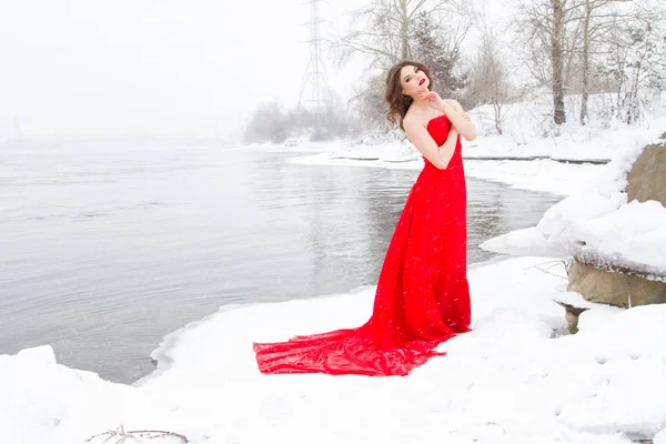 Młoda Dziewczyna Czerwonej Sukience Stoi Brzegu Rzeki Pokrytych Śniegiem — Zdjęcie stockowe