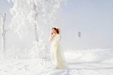 Karla kaplı ağaçlar arka plan üzerinde kırmızı saçlı Genç kız. Kış portresi