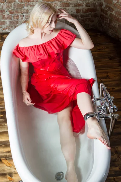 水の風呂に横たわっている長い赤いドレスのブロンド — ストック写真