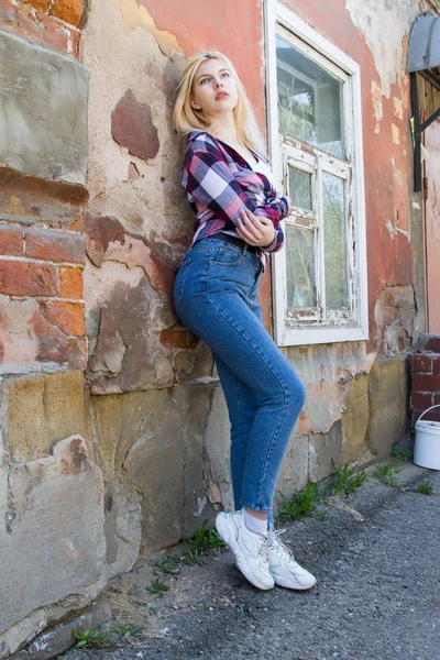 Blonde standing at the wall of a dilapidated house