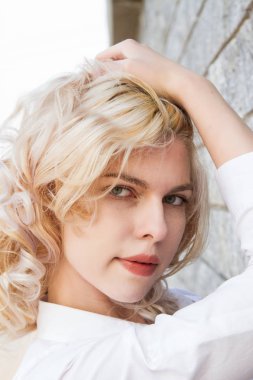 Granit duvarın yanında beyaz gömlekli genç bir sarışın.