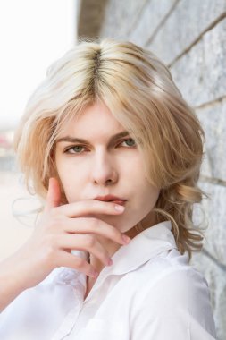 Granit duvarın yanında beyaz gömlekli genç bir sarışın.