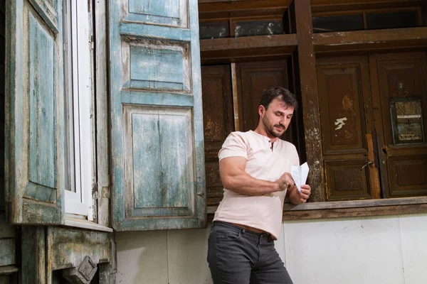 man with a paper airplane against the background of an old wooden house
