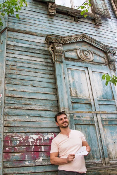 man with a paper airplane against the background of an old wooden house