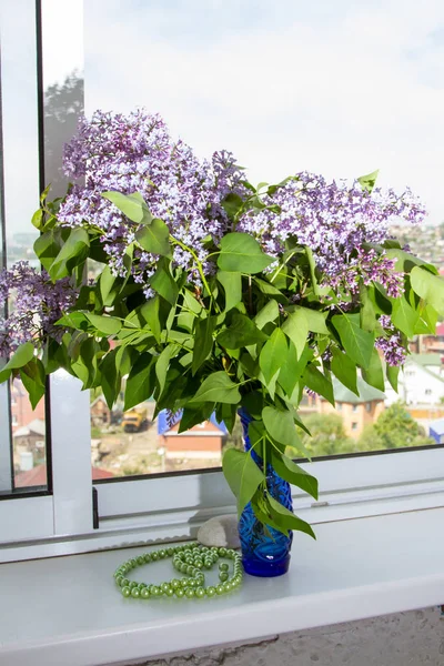 large bouquet of lilacs in a vase on the windowsill