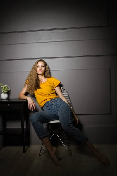 黄色のTシャツとジーンズを着た少女がコーヒーテーブルのそばに座っている — ストック写真