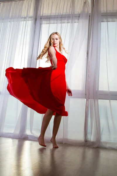 美丽的金发女郎在红色礼服跳舞的窗口背景 — 图库照片