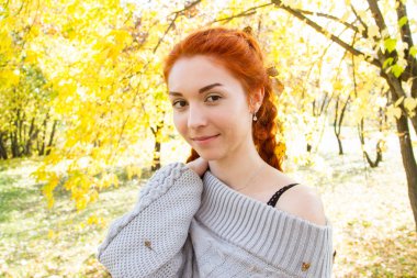 Sonbahar parkında poz veren at kuyruklu kızıl saçlı kız.