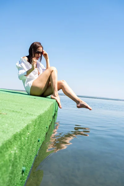 白いシャツを着た少女が水のそばに座り — ストック写真