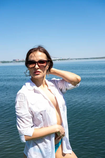 Beyaz tişörtlü kız suyun kenarında oturuyor.