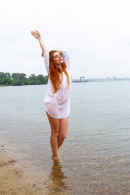 Göletin kıyısında ıslak beyaz gömlekli kızıl saçlı kız.