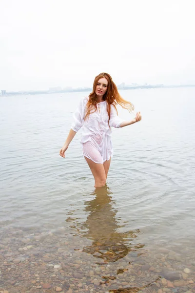池の岸にぬれた白いシャツの赤い髪の少女 — ストック写真