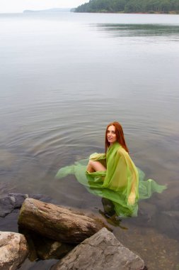 Kızıl saçlı çıplak kız ıslak, şeffaf bir bezle kaplıdır.