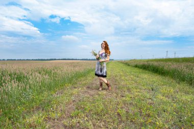 Kırlarda kır çiçeklerinin arasında kızıl saçlı genç bir kız
