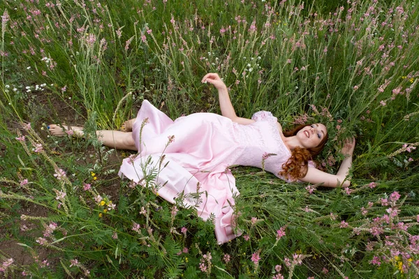 長いピンクのドレスを着た女の子が咲くアルファルファの間の畑にいます — ストック写真