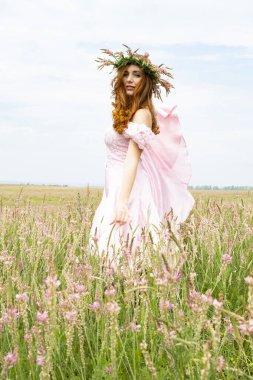 Kafasında çelenkle tarladaki kızıl saçlı kız.
