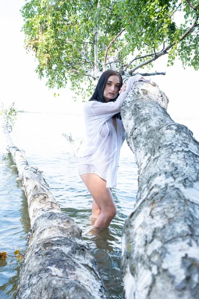 Naked young girl in a wet shirt stands in the water