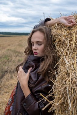Deri ceketli kız saman yığınının yanında duruyor.
