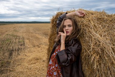 Deri ceketli kız saman yığınının yanında duruyor.