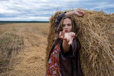 Deri ceketli kız saman yığınının yanında duruyor.